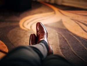 a first person view of men's legs and feet stretched out on a patterned carpet